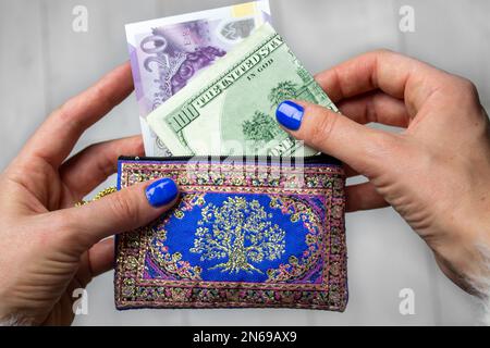 Londra, Regno Unito. 1 maggio 2022 nuovo disegno di legge di 20 sterline britanniche GBP e 100 dollari USA USD in una borsa di donna blu in mani. Economia, finanza, spesa, shopping Foto Stock