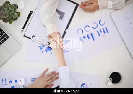 Vista dall'alto di due uomini d'affari che scuotono la mano durante la riunione finanziaria, tabella con il rapporto finanziario e roba. negoziazione aziendale, accordo di successo, un Foto Stock