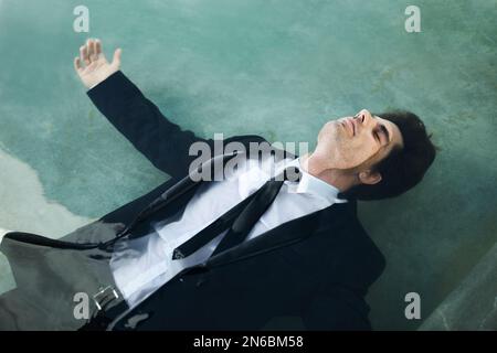 Questa barca sta per affondare... Un giovane uomo d'affari che indossa un abito mentre galleggia in una piscina d'acqua - crisi economica. Foto Stock