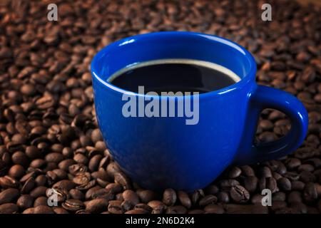 Una tazza di caffè fresco. Tazza blu con una bevanda calda su sfondo scuro. Spazio di copia. Fondo in grani di caffè arrosto. Caffè biologico. Primo piano. Foto Stock