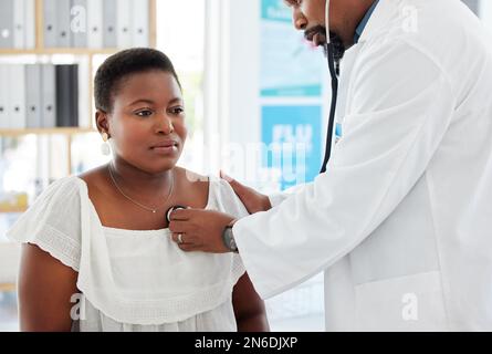 Medico che ascolta i polmoni di un paziente. Medico maturo che usa uno stetoscopio durante un controllo del paziente. Donna afroamericana che ha il suo battito cardiaco Foto Stock