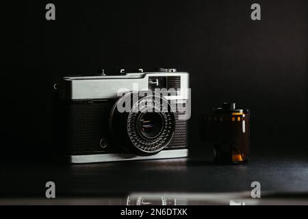 Un primo piano di una vecchia fotocamera retrò con una striscia di pellicola su sfondo nero Foto Stock