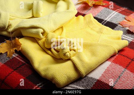 Bel maglione giallo caldo e foglie su plaid a scacchi, primo piano Foto Stock