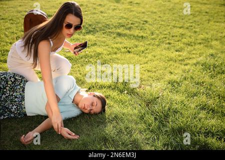 Donna che controlla il polso di una persona inconscia con attacco di cuore nel parco Foto Stock