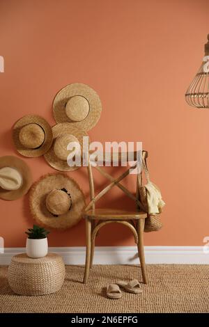 Sedia in legno con borsa e cappelli in paglia su parete marrone. Design degli interni Foto Stock