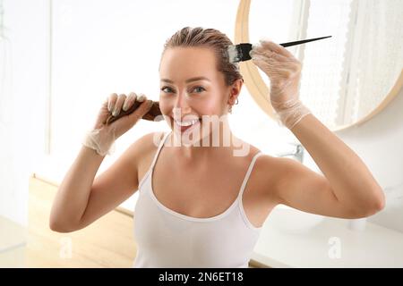 Giovane donna che applica tintura sui capelli in bagno Foto Stock