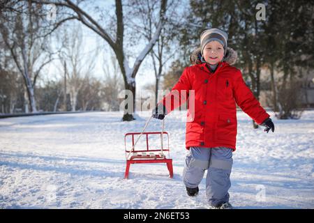 Carino ragazzino con slitta nel parco innevato Foto Stock