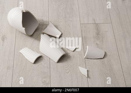 Vaso in ceramica bianco rotto su pavimento in legno Foto Stock