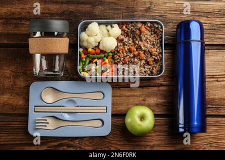 Composizione piana con thermos e portavivande su fondo in legno Foto Stock