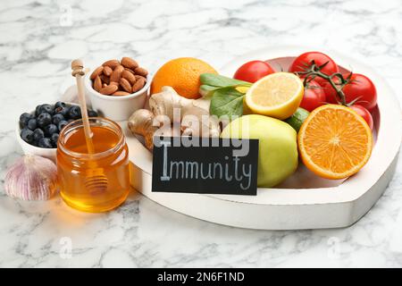 Scheda con parola immunità e prodotti freschi su sfondo marmo chiaro Foto Stock