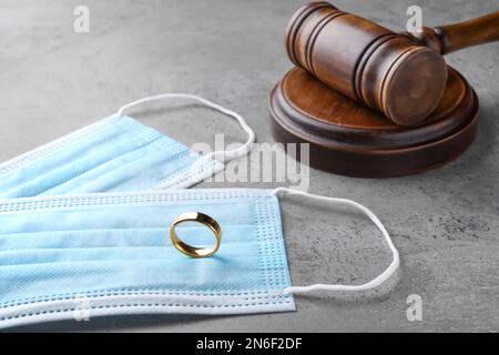 Gavel, maschere protettive e anello di nozze su tavolo grigio. Divorzio durante la quarantena del coronavirus Foto Stock