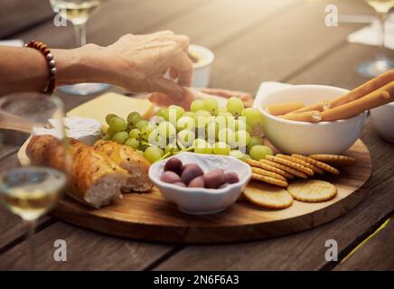Donna sconosciuta che prende da una varietà di spuntini su una tavola di legno di tapas all'esterno. Formaggi, pane, uva fresca e salumi preparati per il pranzo Foto Stock