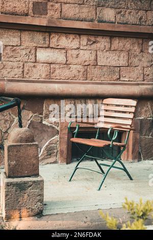 Sedia da giardino pieghevole in metallo con seduta in legno e schienale davanti ad un muro in arenaria di un antico edificio storico, verticale con spazio copia Foto Stock