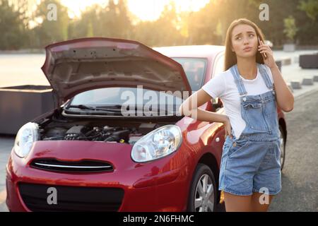 Donna incinta stressata che parla al telefono vicino auto rotta all'aperto Foto Stock