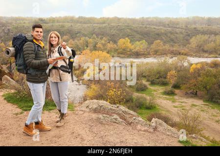 Coppia di viaggiatori con zaini e mappa che godono di una splendida vista vicino al fiume di montagna. Vacanze autunnali Foto Stock