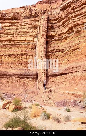 Un lungo e alto dike verticale magmatico igneo taglia attraverso strati orizzontali rossi e arancioni di roccia sedimentaria nel letto del torrente Nahal Ardon a Makhtesh Foto Stock