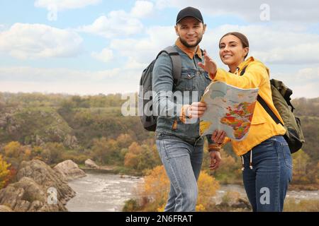 Coppia di viaggiatori con zaini e mappa che godono di una splendida vista vicino al fiume di montagna. Vacanze autunnali Foto Stock