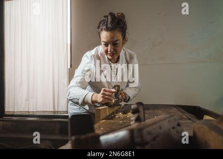 Una lavoratrice di legno con esperienza nella sua 40s sabbie una tavola di legno nella sua officina. È esperta nel restauro di mobili Foto Stock