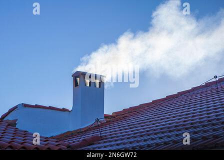 Camino fumoso su un tetto coperto di gelo invernale. sfondo cielo blu Foto Stock