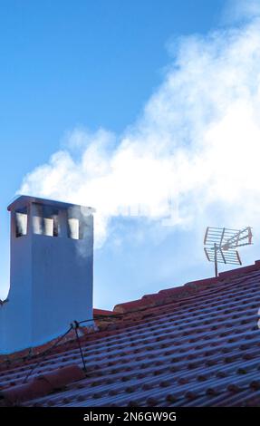 Camino fumoso su un tetto coperto di gelo invernale. sfondo cielo blu Foto Stock