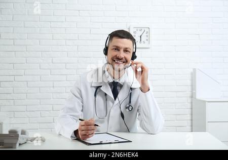 Dottore con cuffia seduto alla scrivania in clinica. Hotline del servizio sanitario Foto Stock