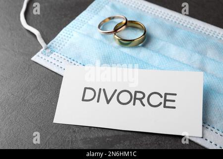 Composizione maschera protettiva e anelli da sposa su tavolo grigio. Divorzio durante la quarantena del coronavirus Foto Stock