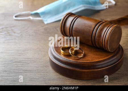 Gavel, anelli di nozze e maschera protettiva sfocata sullo sfondo. Divorzio durante la quarantena del coronavirus Foto Stock