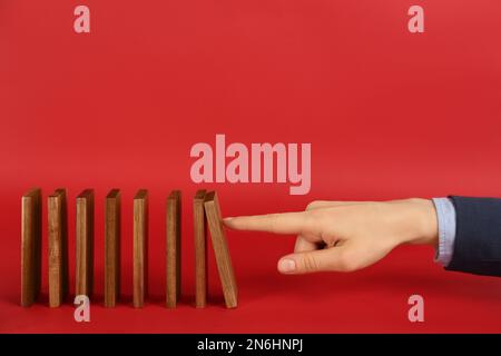 Donna che causa la reazione a catena spingendo tessera domino su sfondo rosso, primo piano. Spazio per il testo Foto Stock