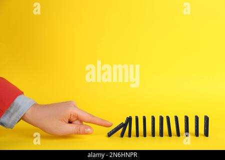 Donna che causa la reazione a catena spingendo tessera domino su sfondo giallo, primo piano. Spazio per il testo Foto Stock