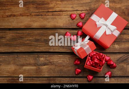 Caramelle al cioccolato a forma di cuore e scatole regalo su tavolo di legno, piatto. Spazio per il testo Foto Stock