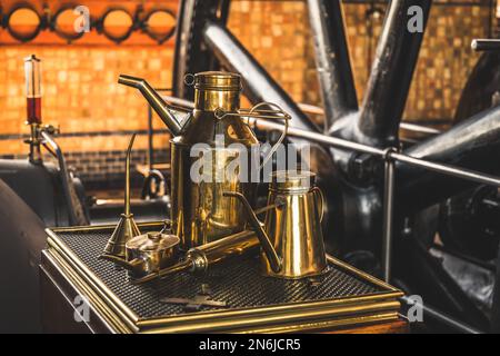 Vecchie lattine di olio in ottone per macchine di lubrificazione. Turbina di un motore a vapore in background. Traduzione del testo 'Lichte Machine Olie' = macchina leggera o Foto Stock