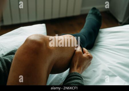 un uomo sta indossando un calzino a compressione seduto sul letto di casa Foto Stock