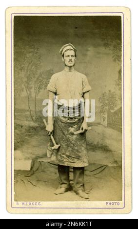 Originale seppia tonata epoca vittoriana CDV (carte de visite o biglietto da visita) di giovane uomo della classe operaia in abiti da lavoro, indossando un cappello di punta come uno chef, commerciante, lavoratore, falegname o muratore con attrezzi, martello, grembiule e cappello. R Hedges 279 High Street, Camden Town, Londra, circa 1878. Foto Stock