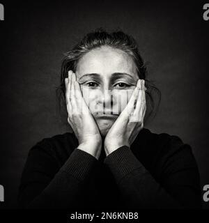 Ritratto concettuale scuro di vecchia donna triste con le mani sopra la testa in brutta grimace. Grana pellicola in bianco e nero. Foto Stock