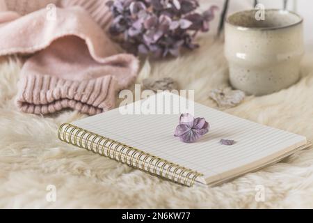 Accogliente scena di pausa caffè con notebook, tazza e tessuto di lana, colori crema e lilla Foto Stock