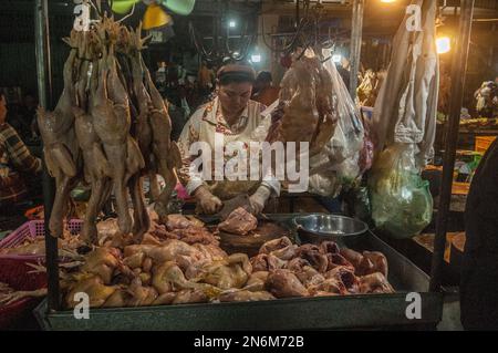 Una femmina cambogiana macellaio taglia pollo crudo al principale mercato all'ingrosso di verdure e carne di notte. Phsar Dumkor, Phnom Penh, Cambogia. © Kraig Lieb Foto Stock