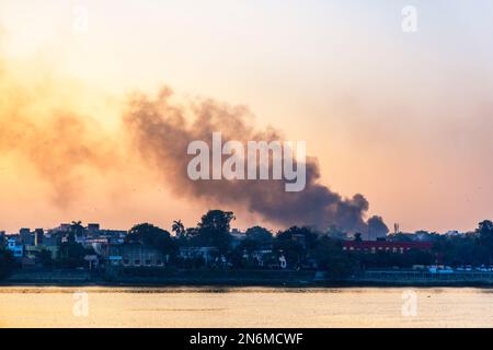 Il fumo spesso inquinante sale al crepuscolo dalle rive del fiume Hooghly aggiungendo allo smog e la scarsa qualità dell'aria vicino Calcutta, Bengala Occidentale, India Foto Stock