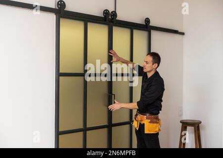 Un bel giovane uomo che installa la doppia porta scorrevole del patio dentro un nuovo cantiere Foto Stock