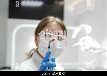 Il dentista ha estratto il dente malato dal paziente in studio dentale. Focus su pinze dentali in acciaio inox e dente inferiore estratto in esso dentista donna dottore in possesso di un dente coperto di sangue Foto Stock