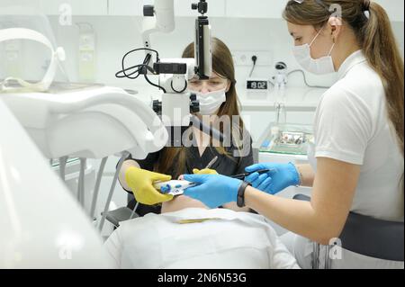 moderna clinica odontoiatrica processo di riempimento del canale radicolare utilizzando il microscopio altra ultima tecnologia medico infermiere aiutare il paziente con dentifricio riempimento protesi Foto Stock