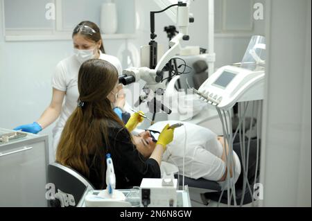 Attrezzatura odontoiatrica moderna tecnica di applicazione di guanti da dentista femmina con microscopio dentale per esaminare i denti dei pazienti medico paziente assistente dentistico tr Foto Stock