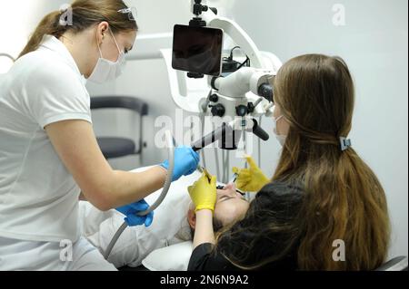 Attrezzatura odontoiatrica moderna tecnica di applicazione di guanti da dentista femmina con microscopio dentale per esaminare i denti dei pazienti medico paziente assistente dentistico tr Foto Stock