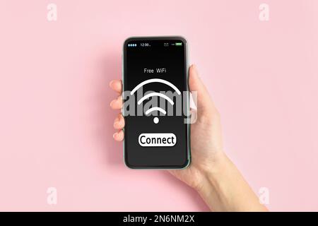 Donna che si connette al WiFi utilizzando il telefono cellulare su sfondo rosa, primo piano Foto Stock