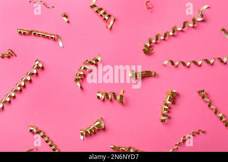 Streamers a serpentina dorati lucidi su fondo rosa, giacitura piatta Foto Stock