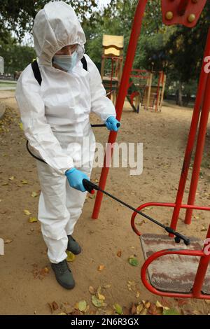 Donna che indossa tuta di protezione chimica con spruzzatore disinfettante nel parco giochi. Misura preventiva durante la pandemia di coronavirus Foto Stock