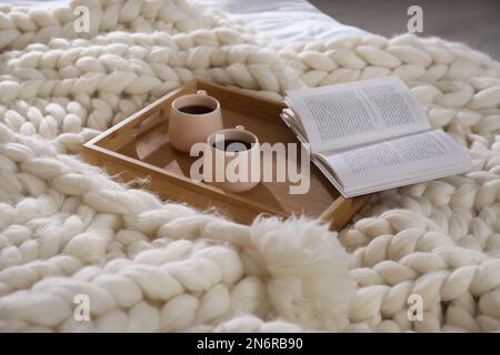 Vassoio in legno con coppe e libro su plaid a maglia bianca Foto Stock