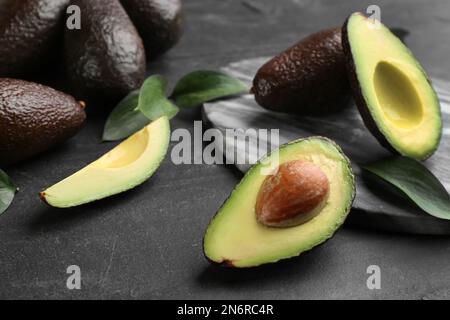 Avocado intero e tagliato con foglie verdi su tavola nera Foto Stock