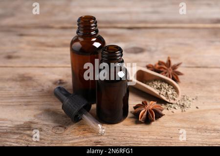 Bottiglie di olio essenziale, anice e semi su tavola di legno Foto Stock