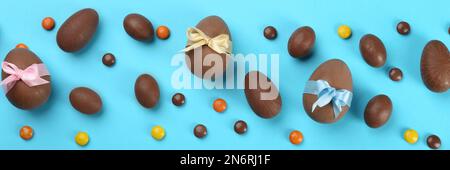 Uova di cioccolato dolce e caramelle luminose su sfondo azzurro, piatto. Design del banner Foto Stock