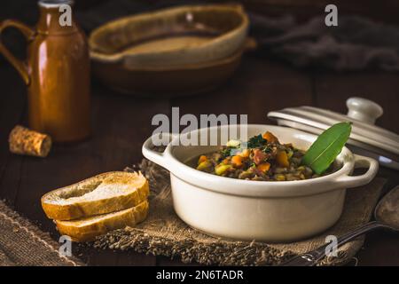Ciotola di stufato di lenticchie, pane tostato e foglia di alloro su un tavolo rustico in legno Foto Stock